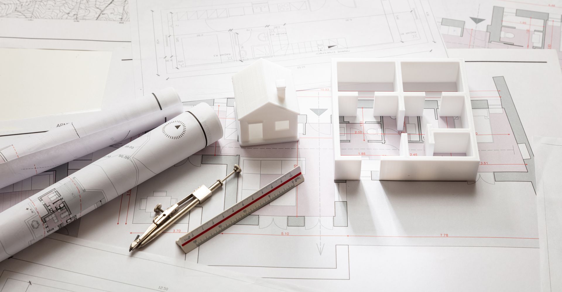 Plans architecturaux avec plans enroulés, stylos et une petite maquette blanche du bâtiment sur un bureau.