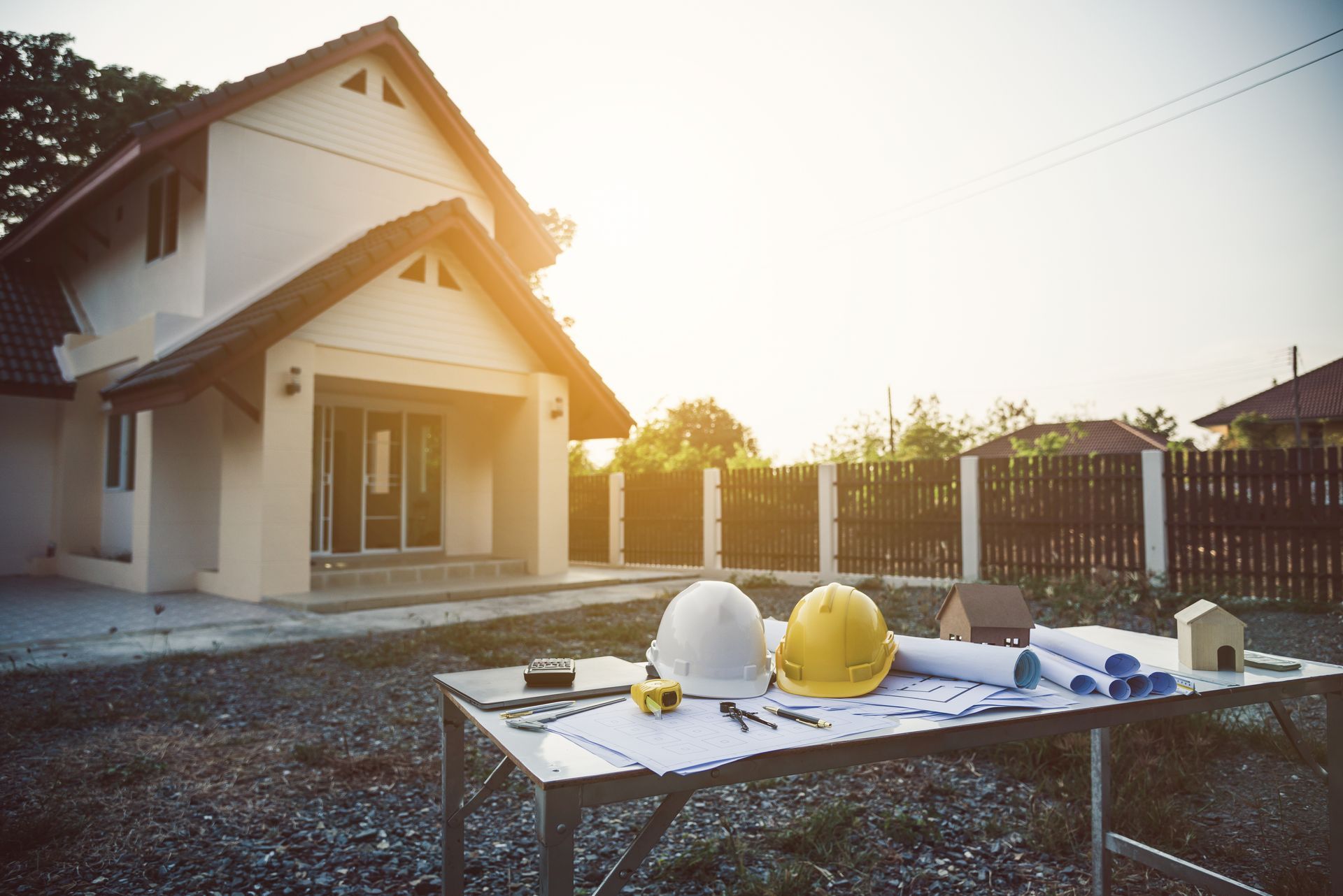 Maison en construction avec des casques et des outils sur une table au premier plan au coucher du soleil.