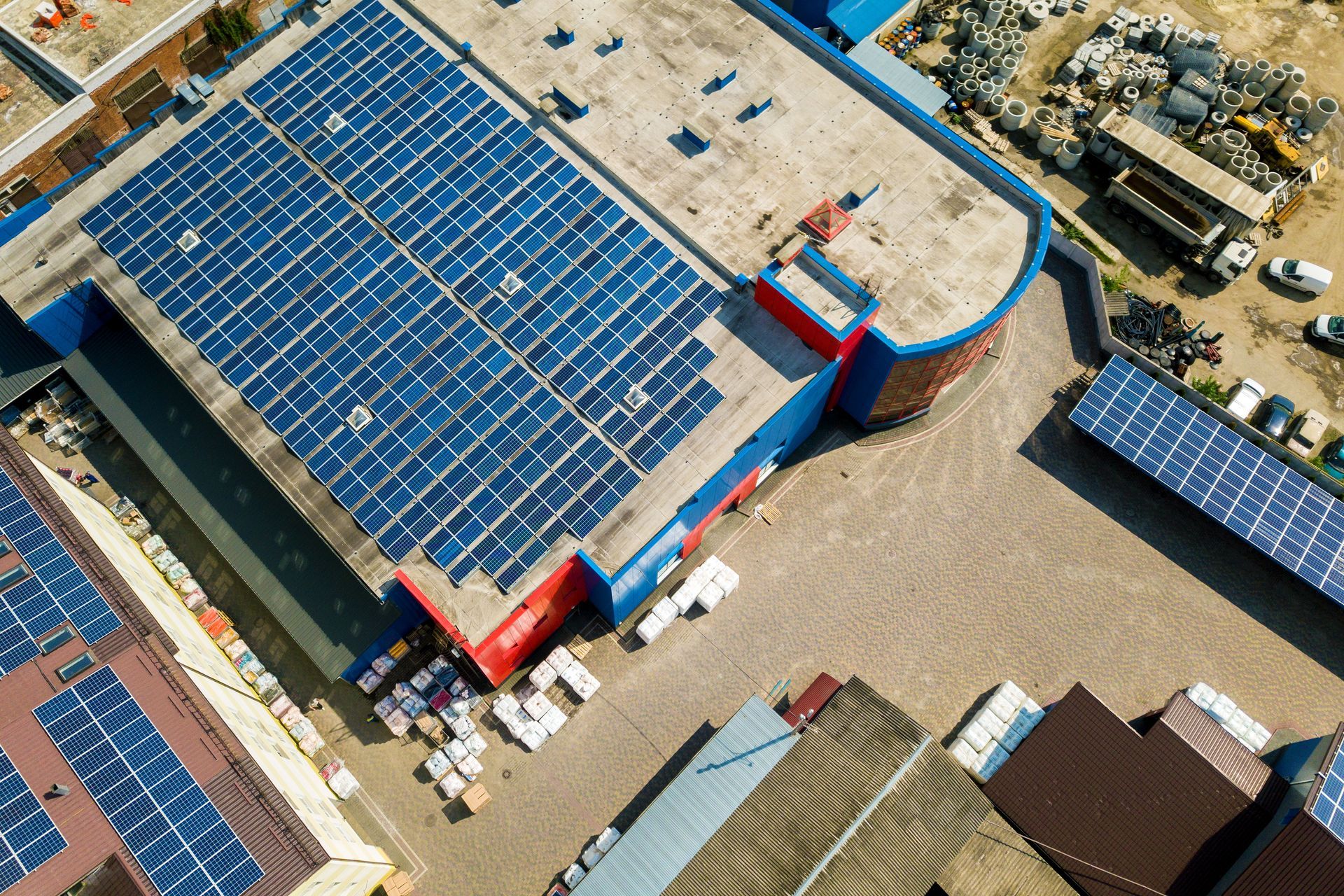 Vue aérienne d'un grand bâtiment avec des panneaux solaires bleus sur le toit, situé dans une zone industrielle.