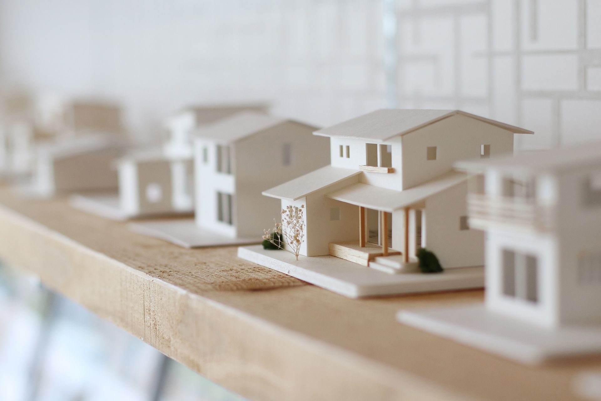 Maisons miniatures sur une surface en bois, avec une petite maison blanche moderne au premier plan.