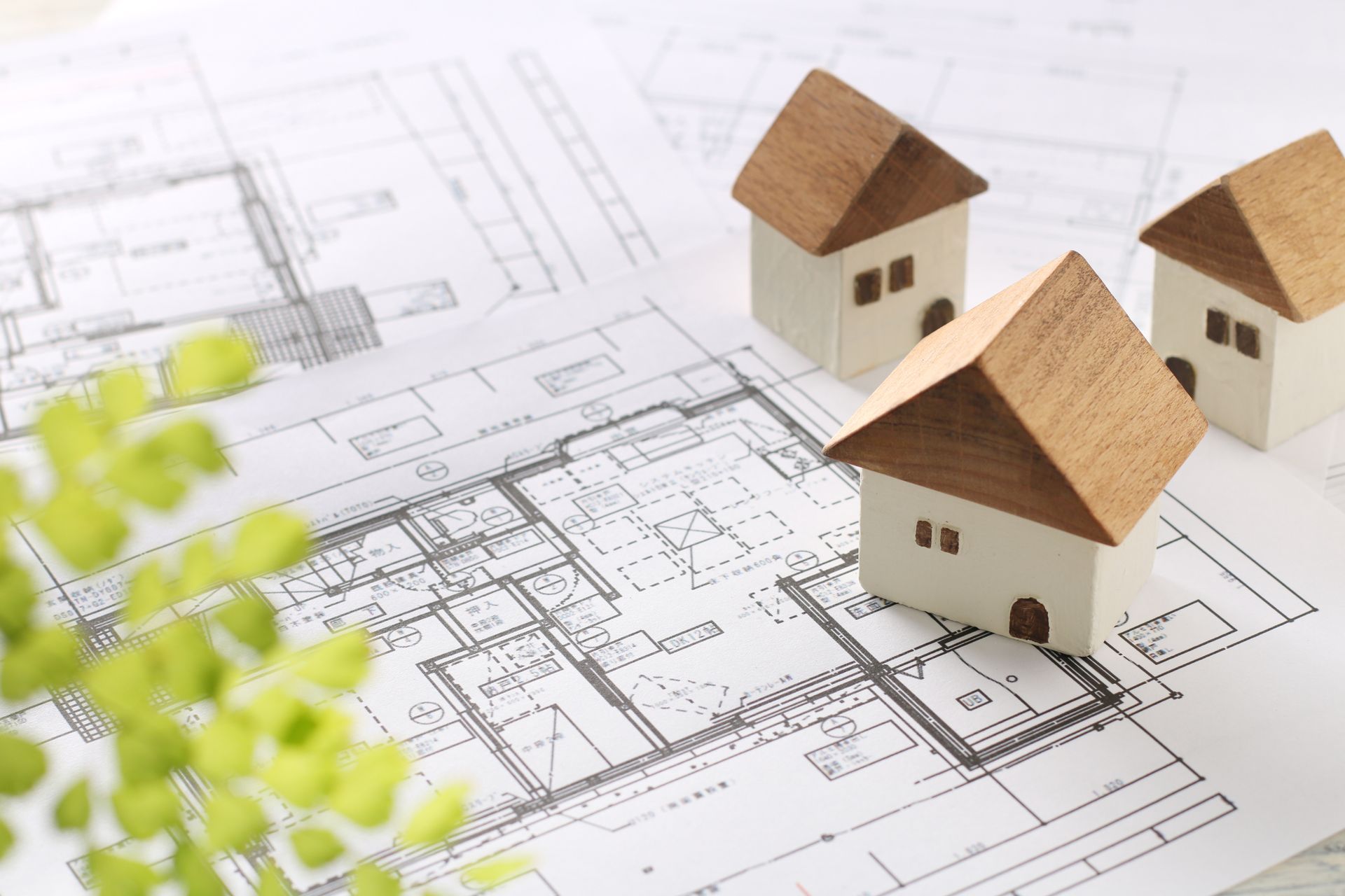 Maisons miniatures sur des plans architecturaux avec une petite plante verte au premier plan.