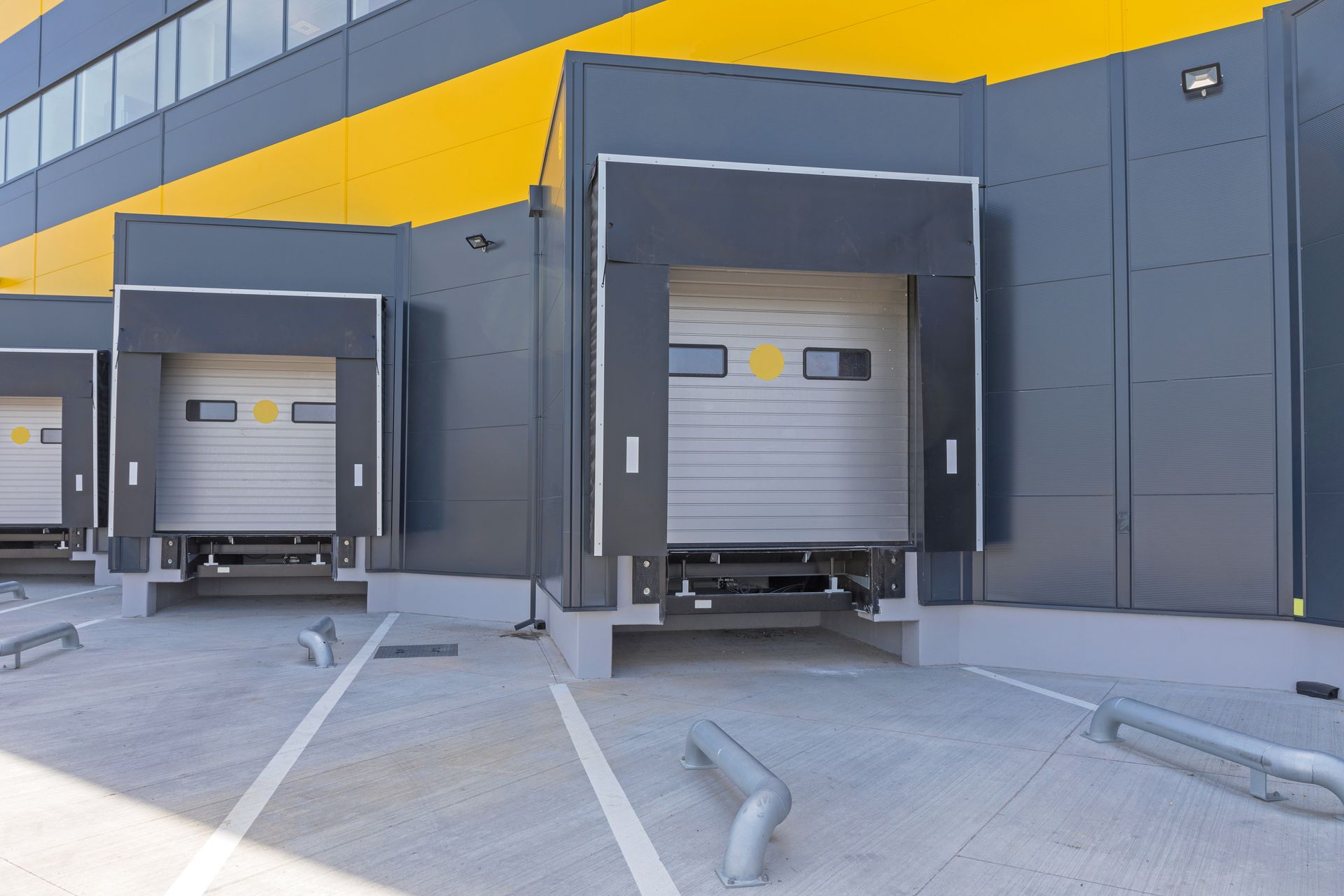 Trois quais de chargement sur un bâtiment industriel gris avec des garnitures jaunes et des remorques stationnées.