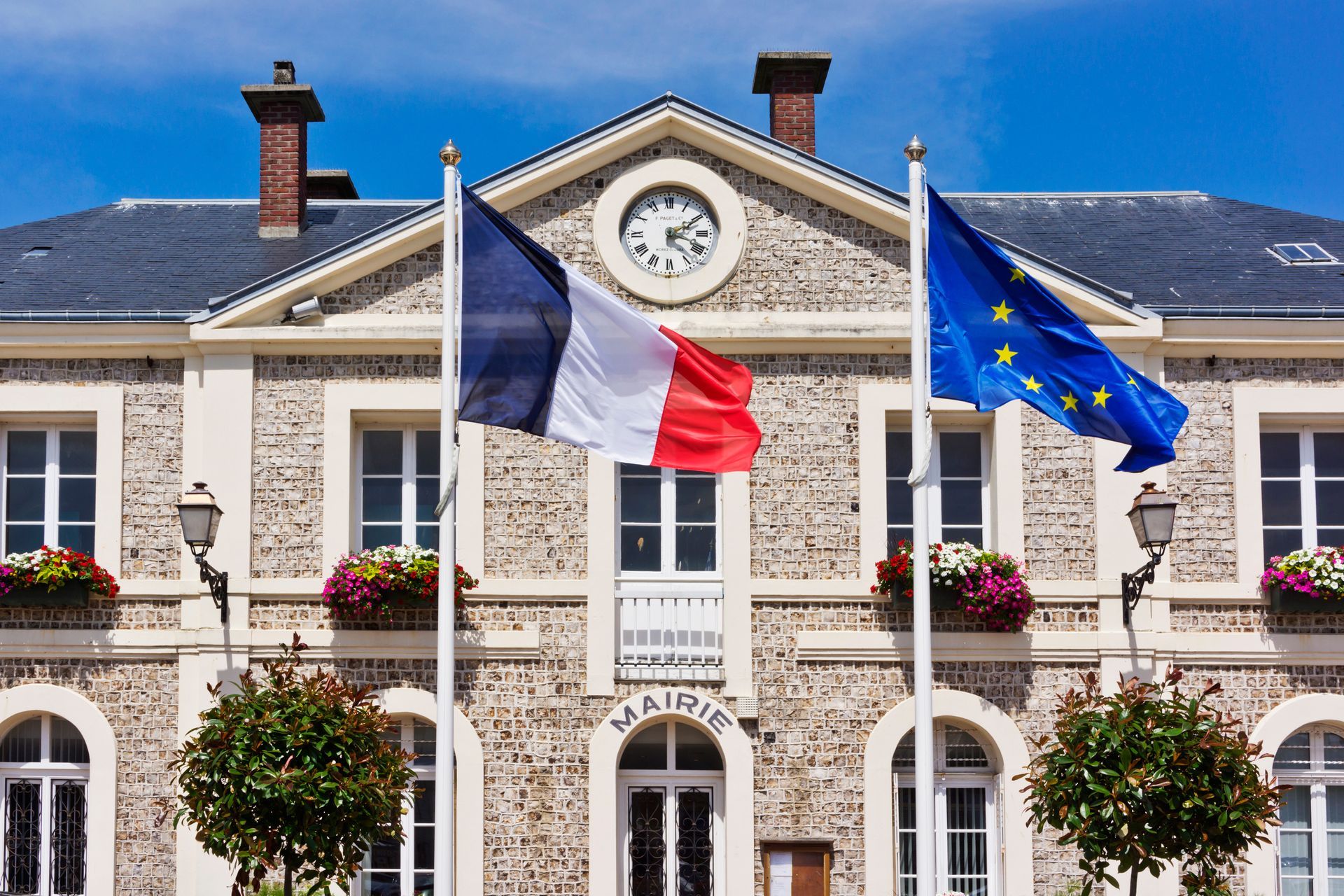 Hôtel de ville français avec les drapeaux français et européen flottant devant une façade en pierre.