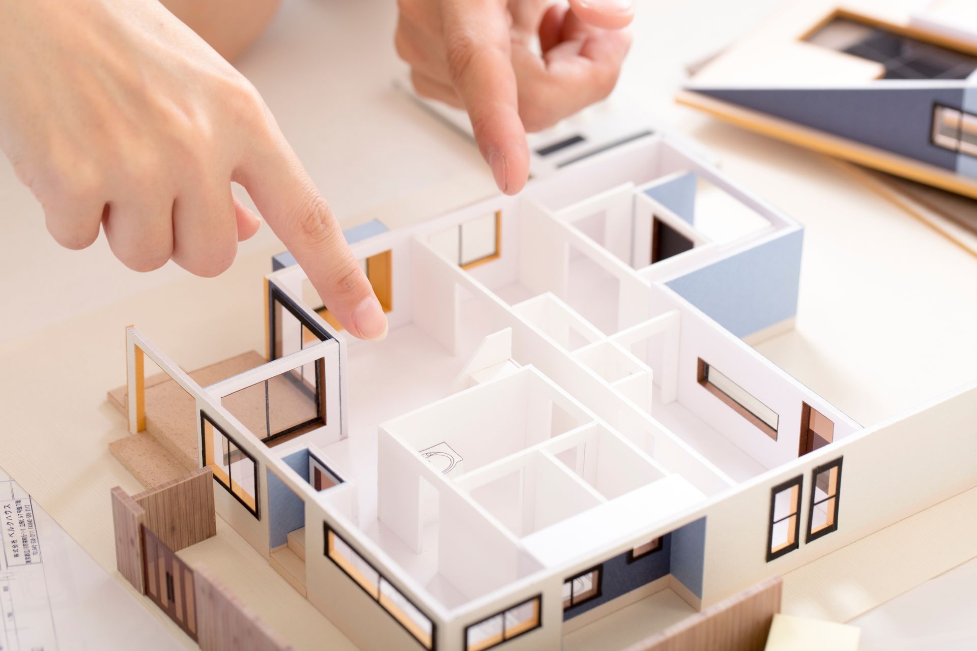 Des mains pointent du doigt un plan de maison avec des murs intérieurs blancs et des cadres de fenêtres noirs.