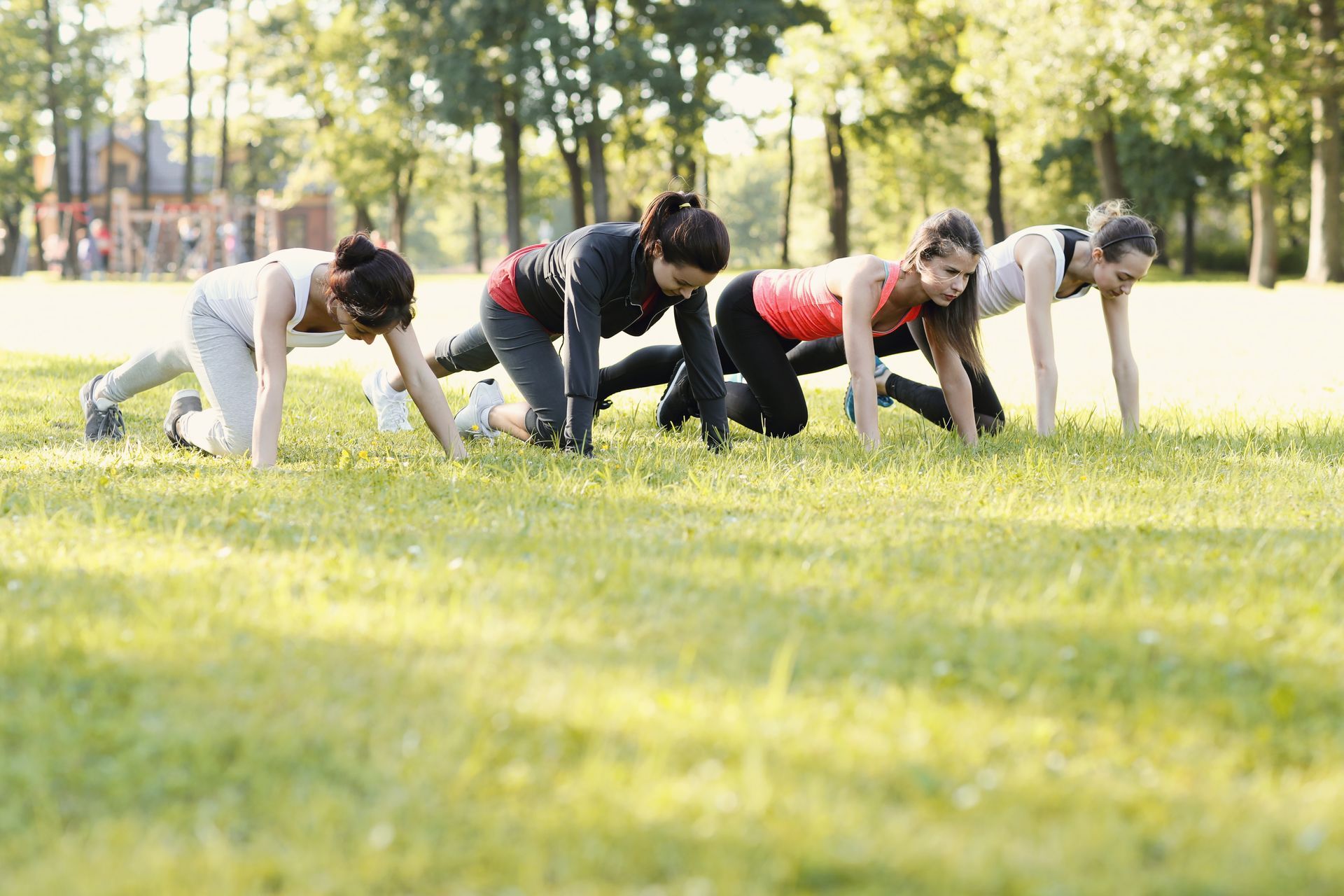 Mujeres en un parque haciendo un ejercicio de plancha sobre el césped, clase de fitness.