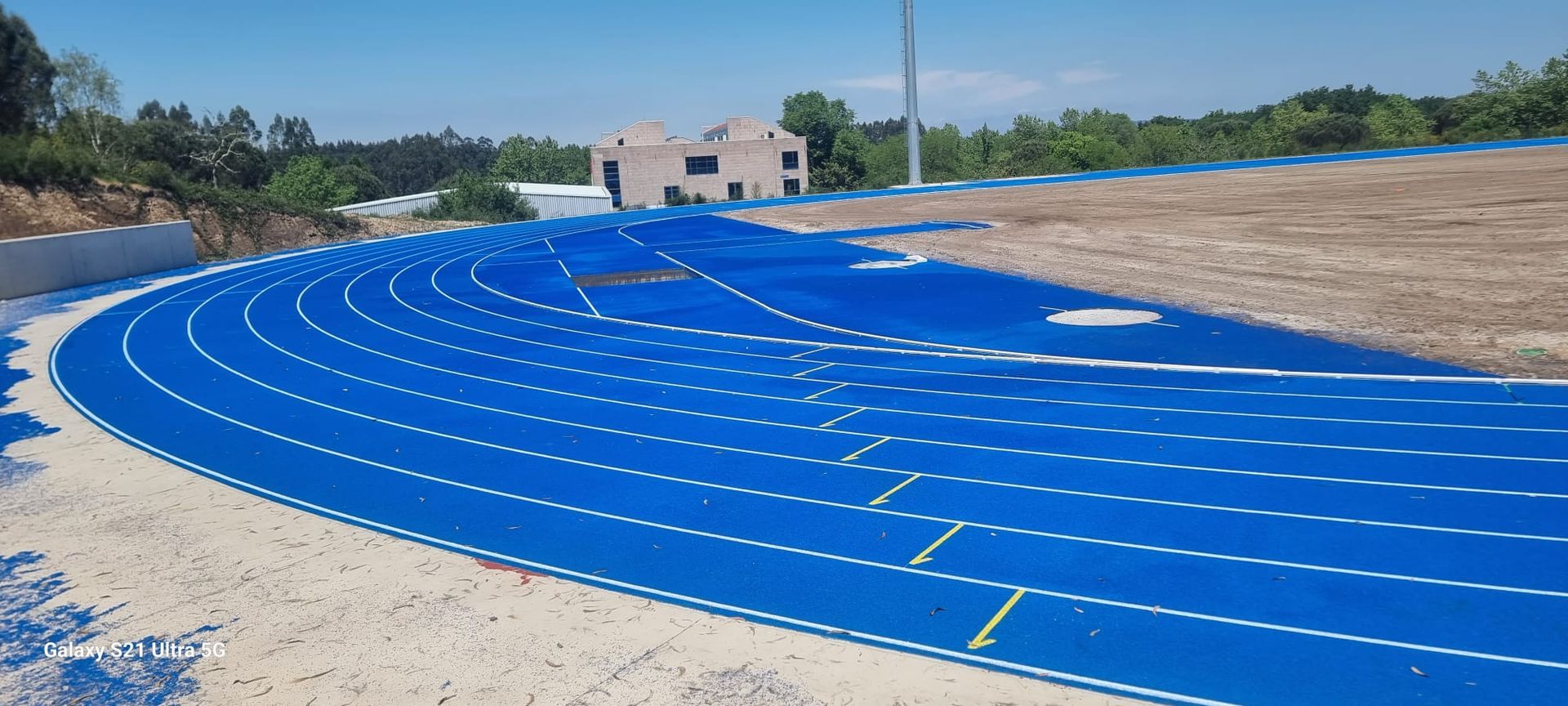 Se está construyendo una pista azul en un campo con un edificio al fondo.