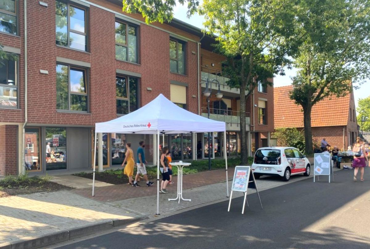 Eine Gruppe von Menschen steht unter einem weißen Zelt vor einem Gebäude.