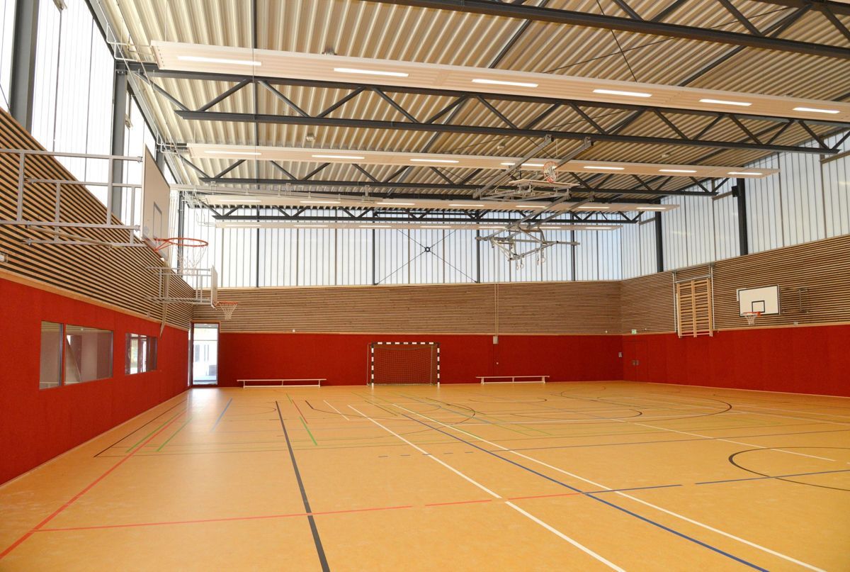 Eine große Turnhalle mit Basketballkorb und Volleyballnetz.
