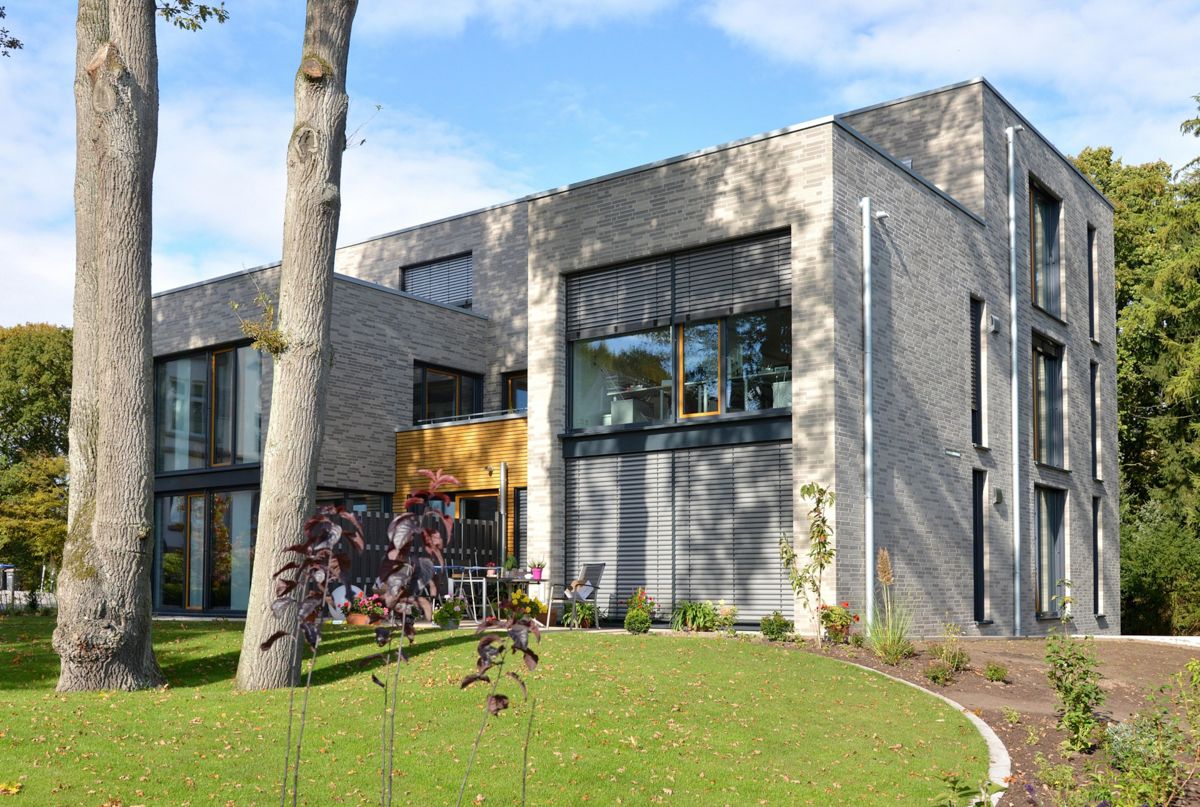 Ein großes Backsteingebäude mit vielen Fenstern ist von Bäumen umgeben.