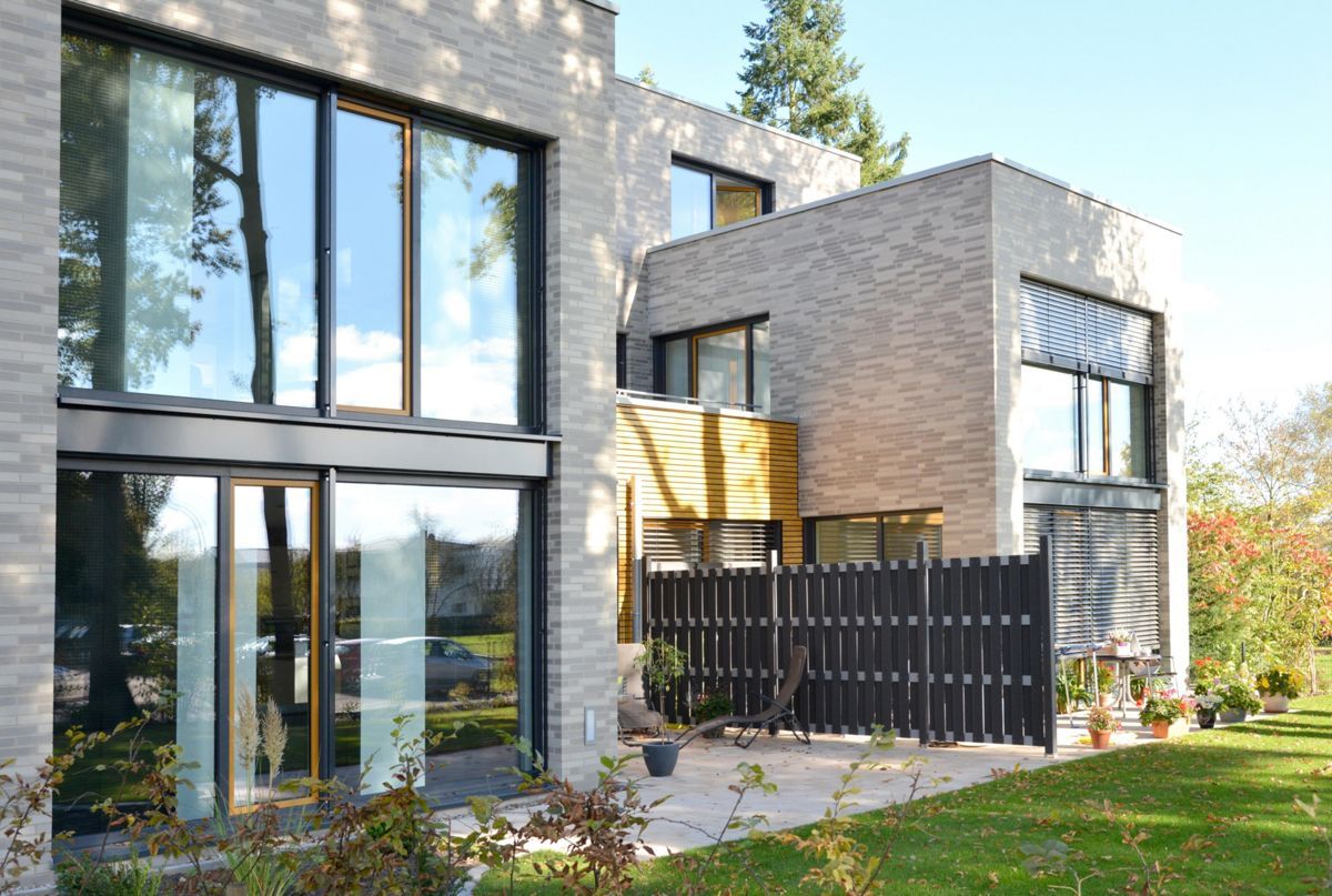 Ein modernes Backsteinhaus mit vielen Fenstern und einem Zaun davor.