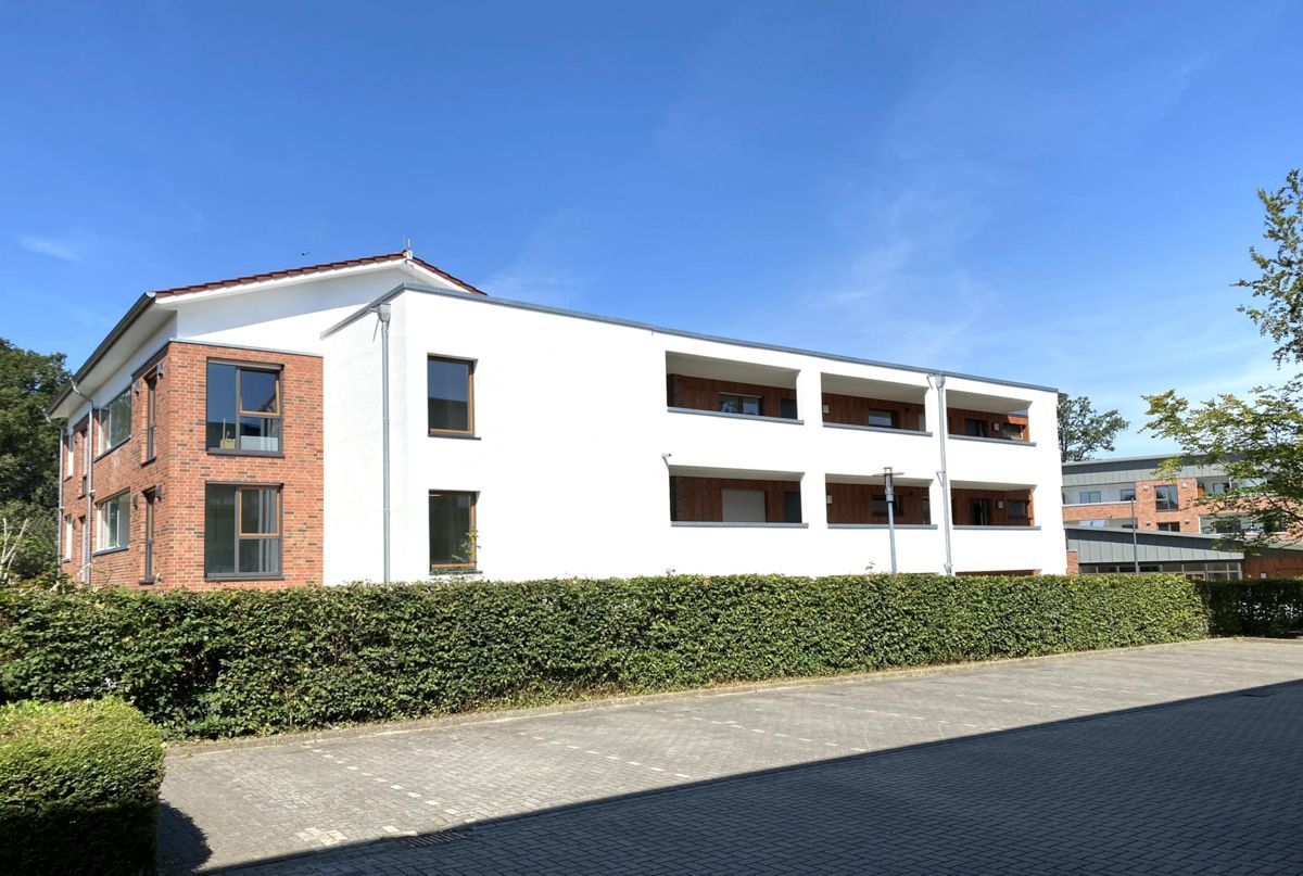 Ein großes weißes Gebäude mit einer Backsteinfassade ist von einer Hecke umgeben.
