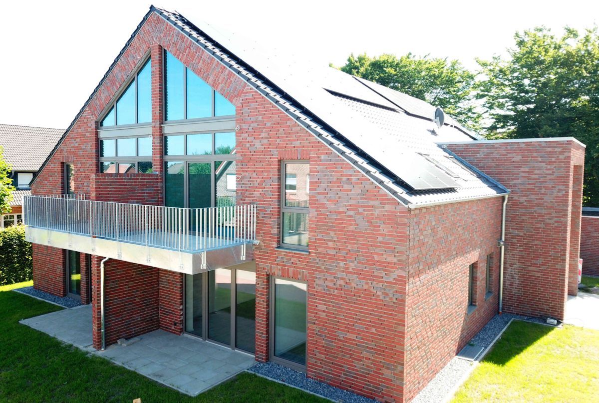 Ein großes rotes Backsteinhaus mit Balkon und Solarzellen auf dem Dach.