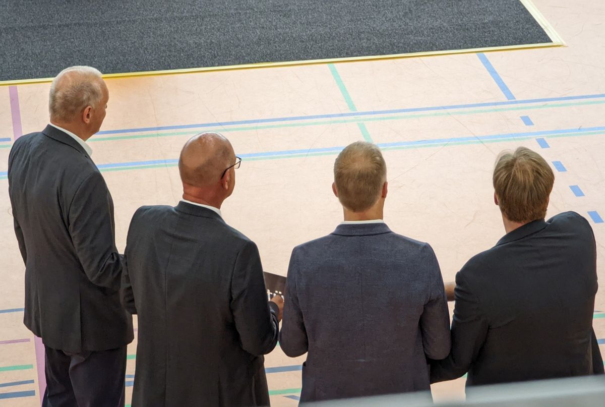 Eine Gruppe von Männern in Anzügen steht vor einem Basketballplatz.