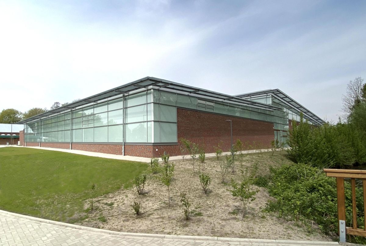 Ein großes Gebäude mit vielen Fenstern ist von Gras und Bäumen umgeben.