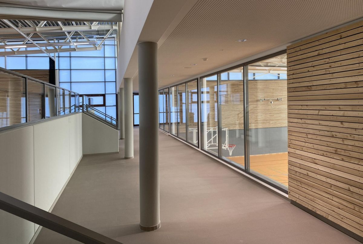 Ein langer Flur in einem Gebäude mit einem Basketballplatz im Hintergrund.