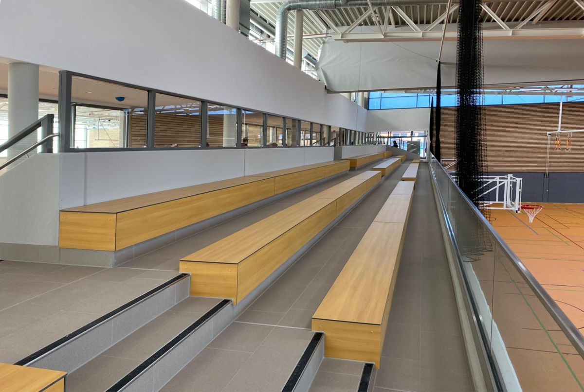 Eine Reihe von Holzbänken in einer Turnhalle mit einem Basketballplatz im Hintergrund