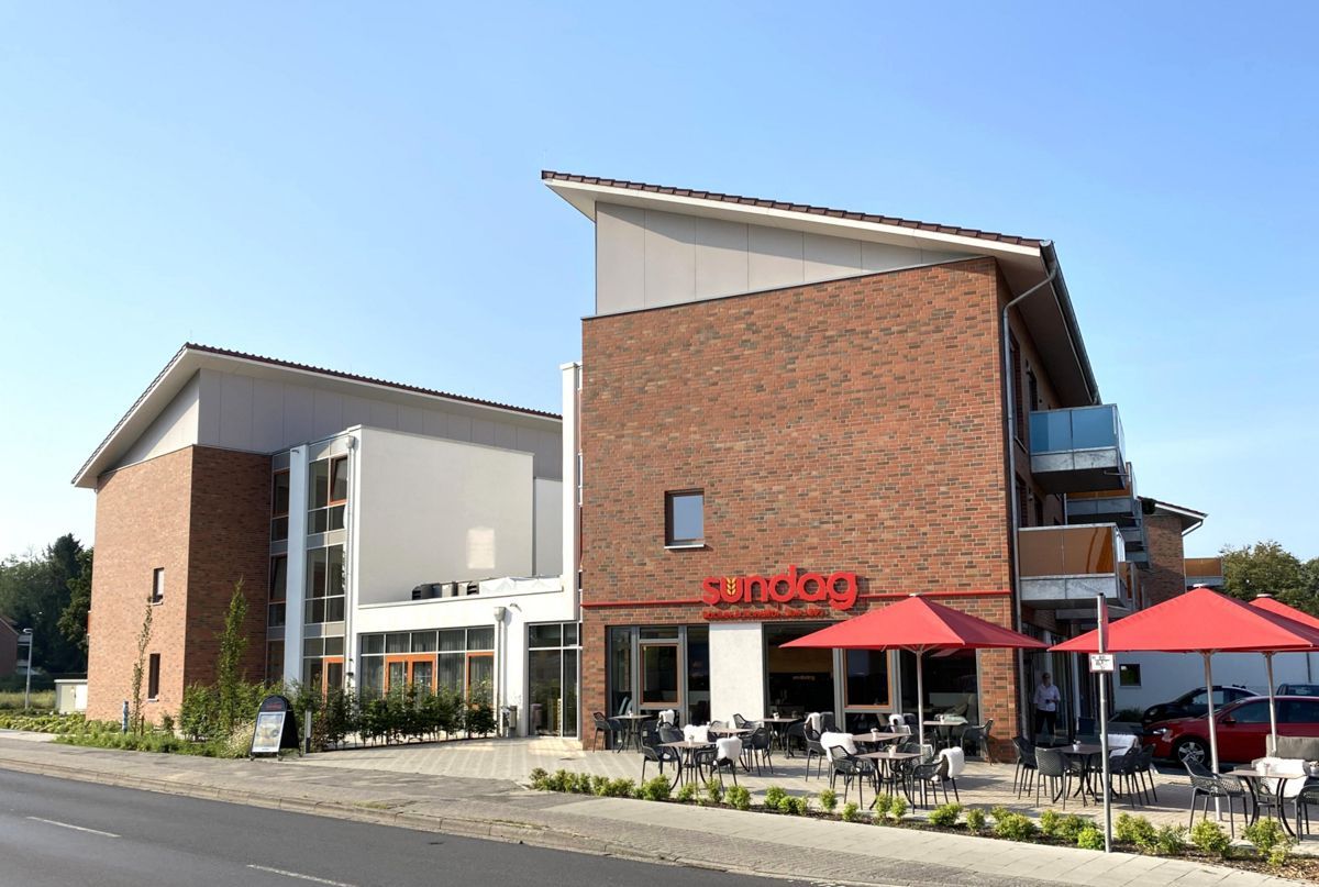 Ein großes Backsteingebäude mit Tischen und Sonnenschirmen davor