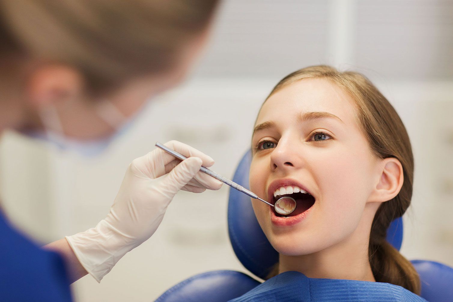 Una mujer está sentada en una silla dental mientras un dentista le examina los dientes.