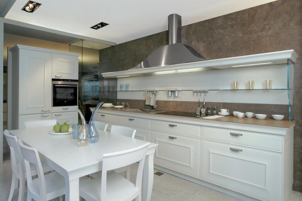 Eine Küche mit weissen Schränken und einem Tisch und Stühlen. Foto von Sandro Luisi Küchenbau
