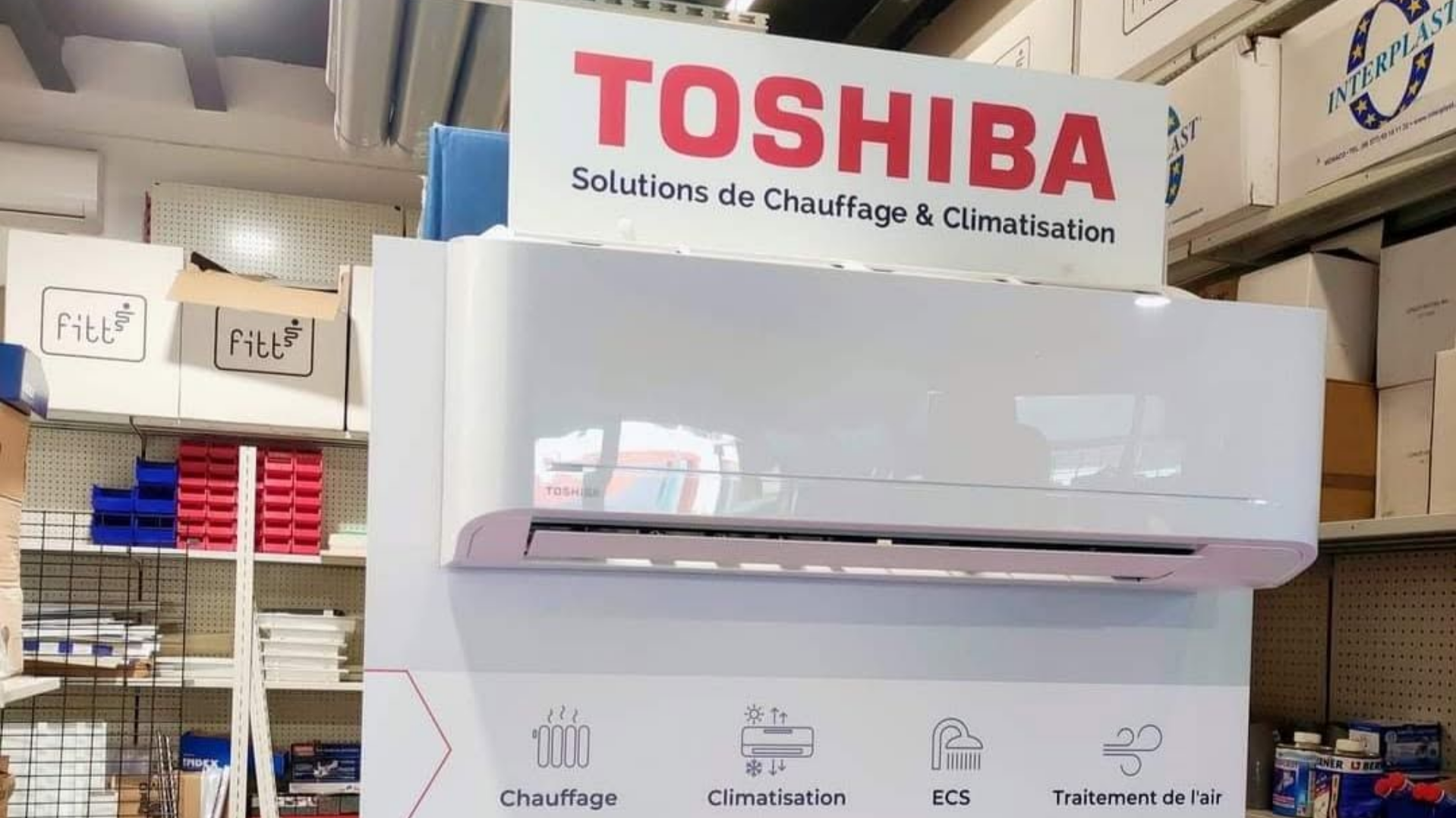 Climatiseur mural blanc Toshiba exposé en magasin, avec logo rouge et signalétique espagnole au-dessus.