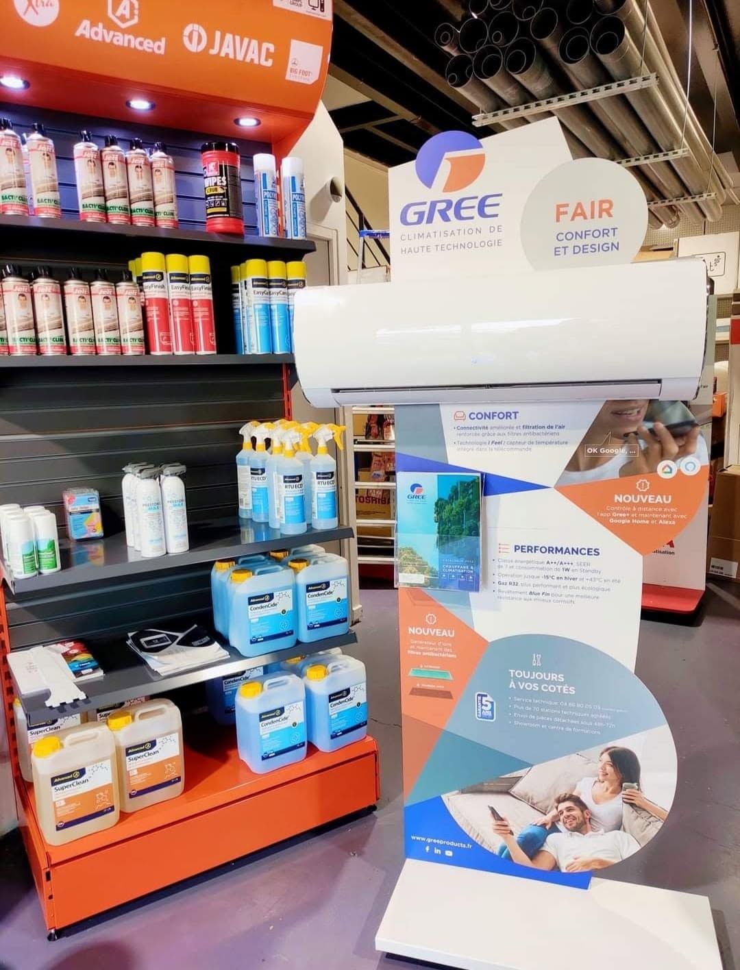 Présentoir de climatiseurs dans un magasin, arborant les logos GREE et Fair, à côté des rayons d'électroménager et de boissons.