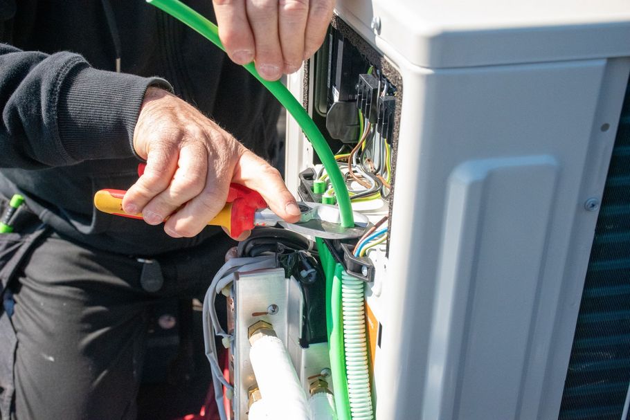 Un technicien raccorde des câbles verts à l'intérieur d'une armoire électrique ouverte.