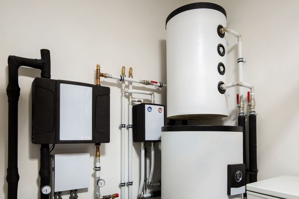 Chauffe-eau mural blanc avec tuyaux et vannes noirs dans une buanderie
