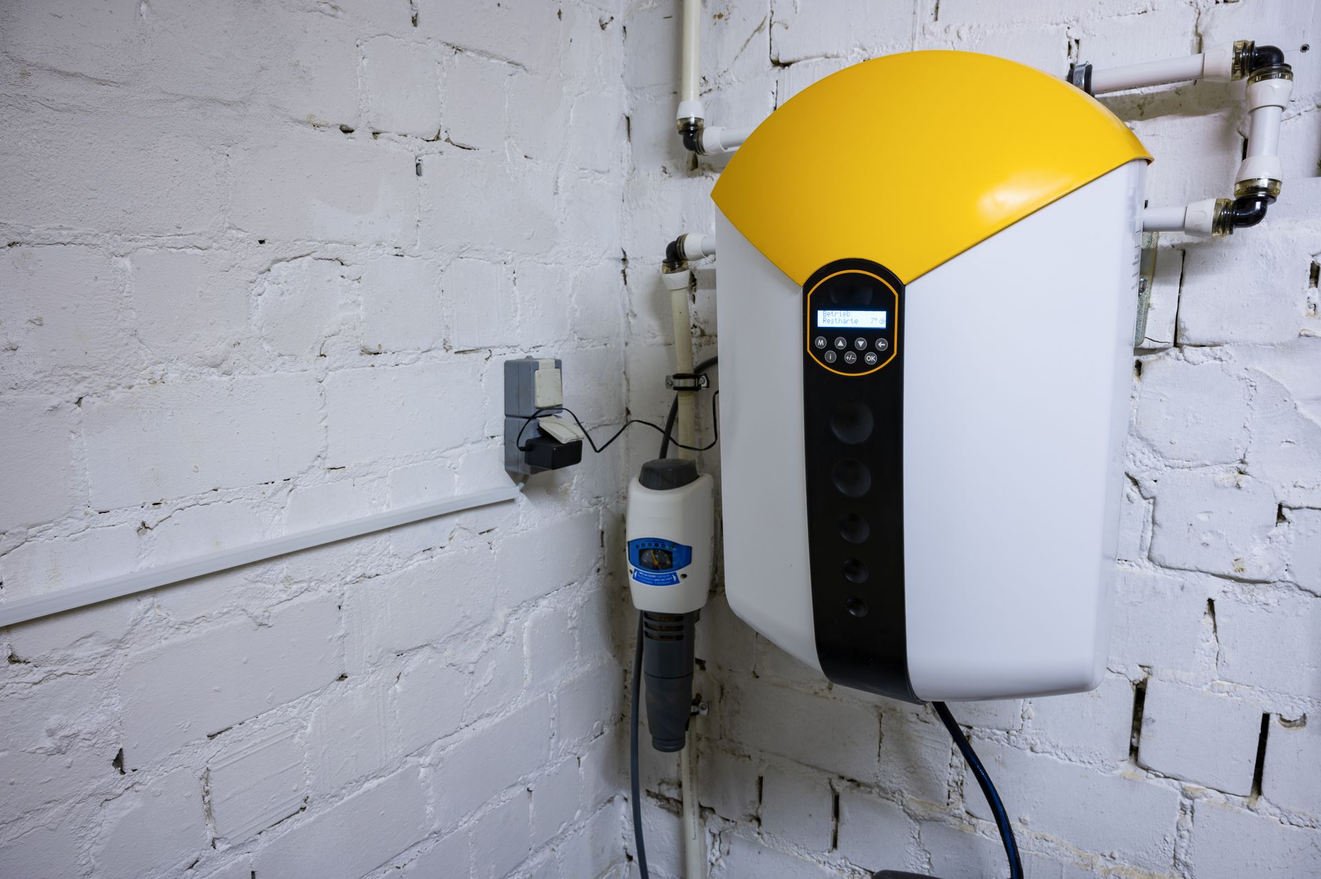 Borne de recharge murale blanche et jaune pour véhicules électriques, installée dans un local technique en briques, avec câble et prise de courant.
