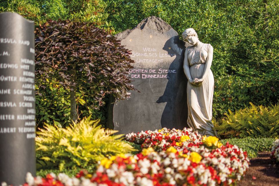 Grabmal und Frauenstatue in bepflanzter Fläche