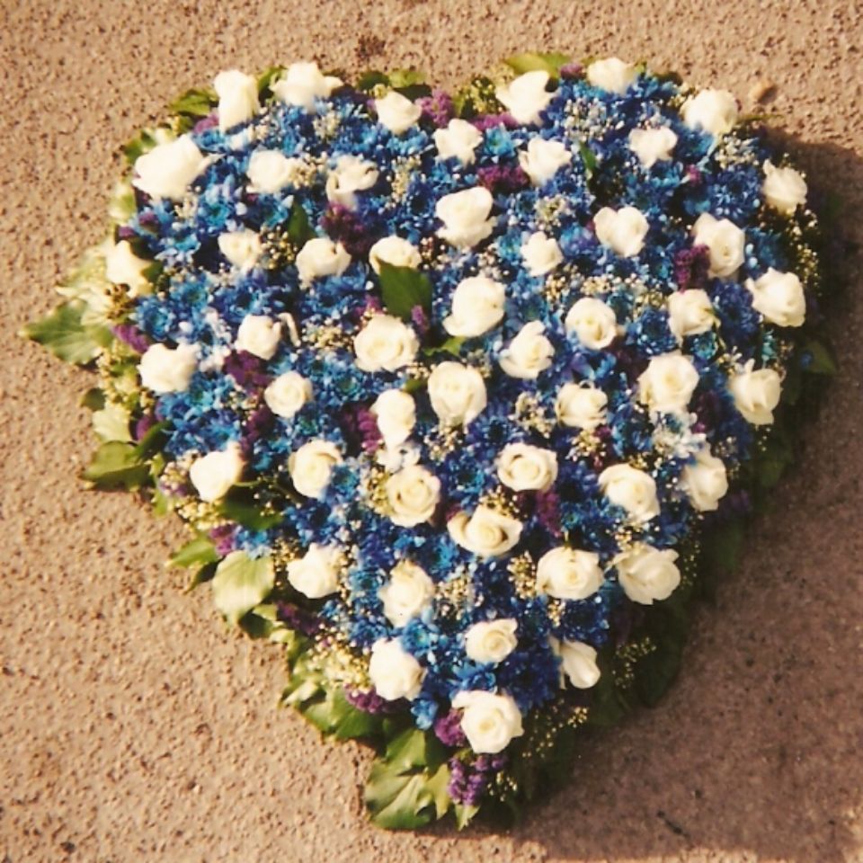 herzförmiges Blumengesteck mit weißen Rosen und blauen Blüten