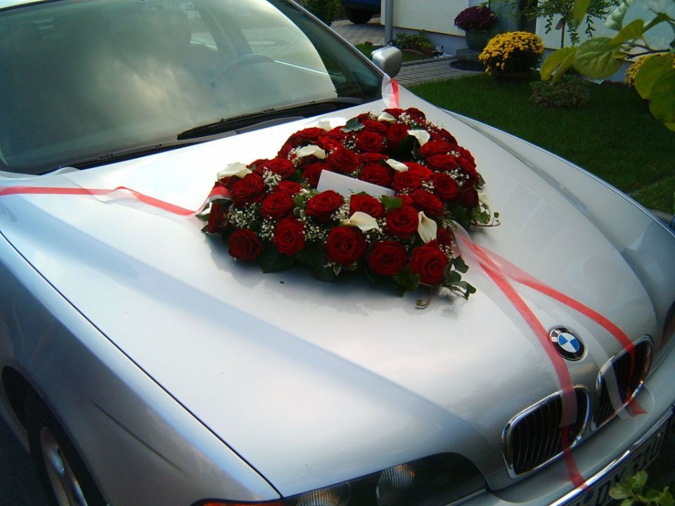 Hochzeitsschmuck auf einem Auto mit roten Rosen und weißen Lilien