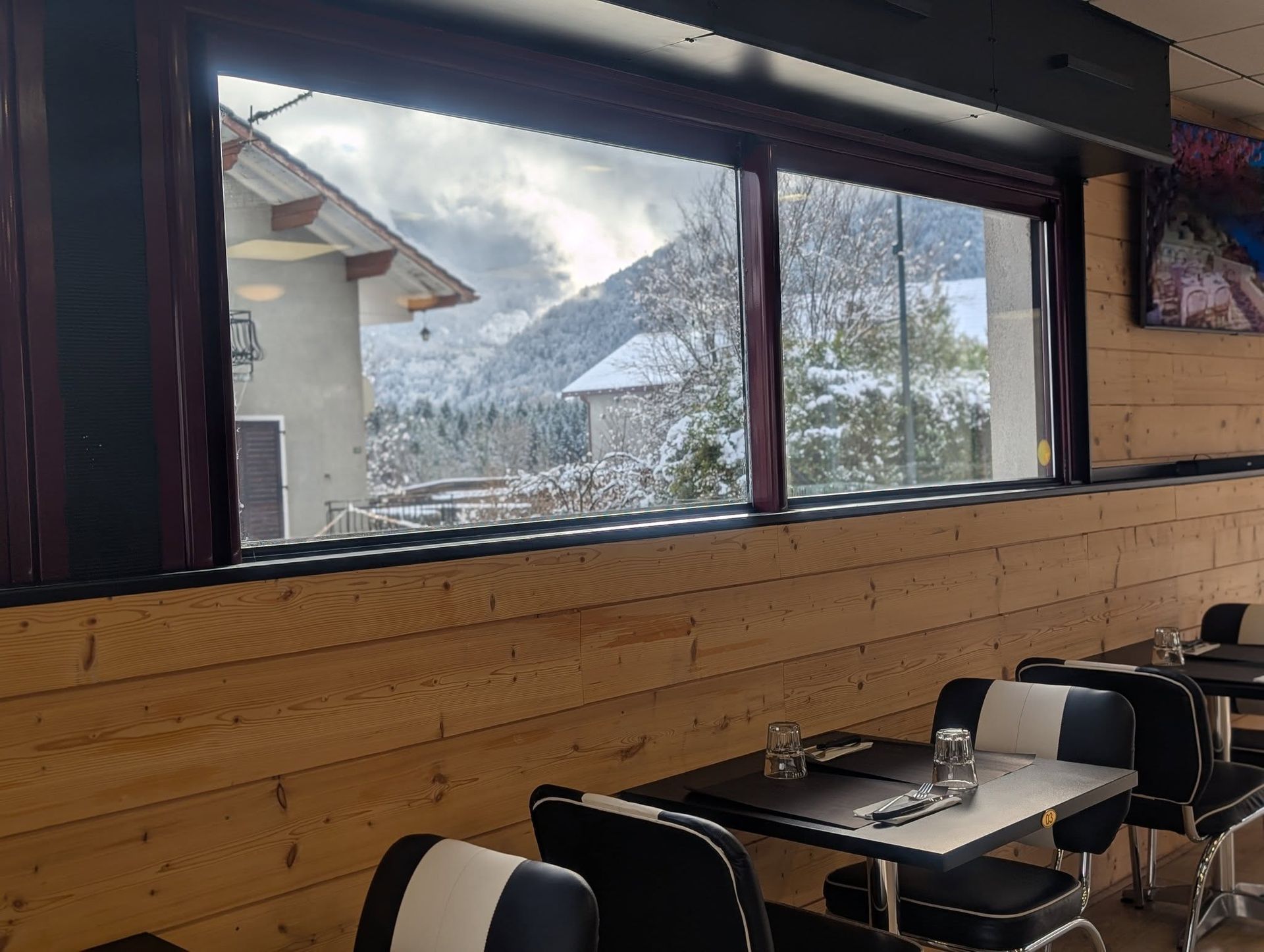 Intérieur d'un restaurant avec vue sur les montagnes enneigées. Tables et chaises au premier plan.