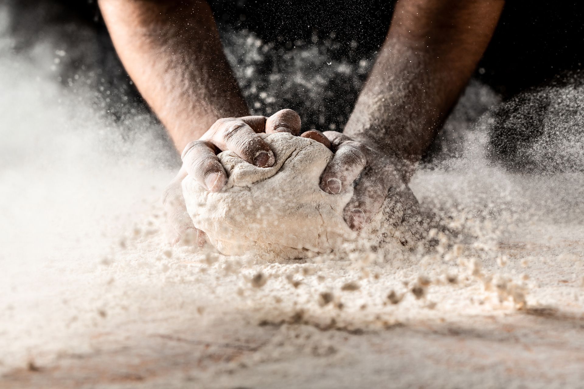 Des mains pétrissent la pâte, la farine tourbillonne autour d'elles.