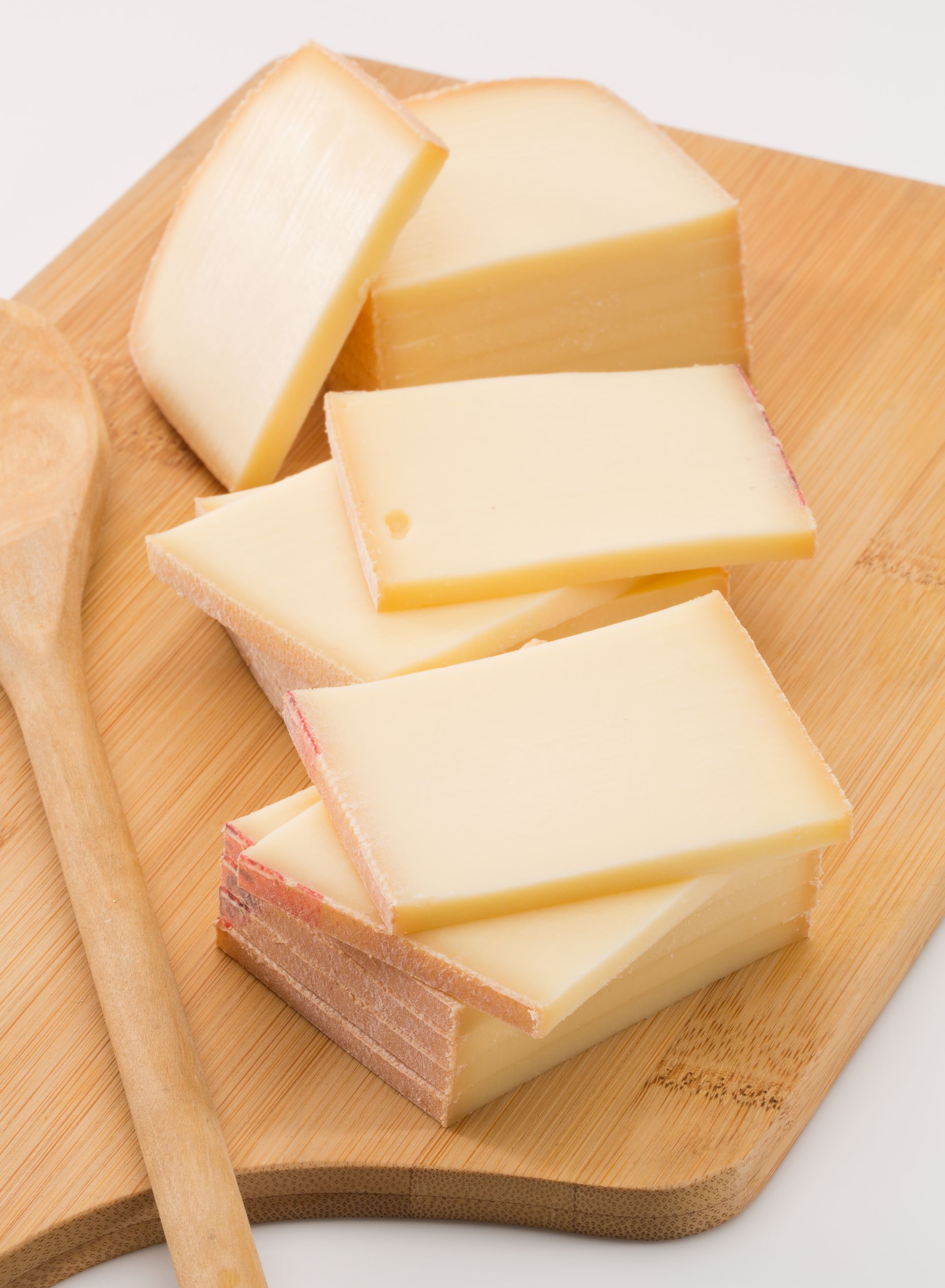 Blocs et tranches de fromage jaunâtre sur une planche à découper en bois, avec une cuillère en bois.