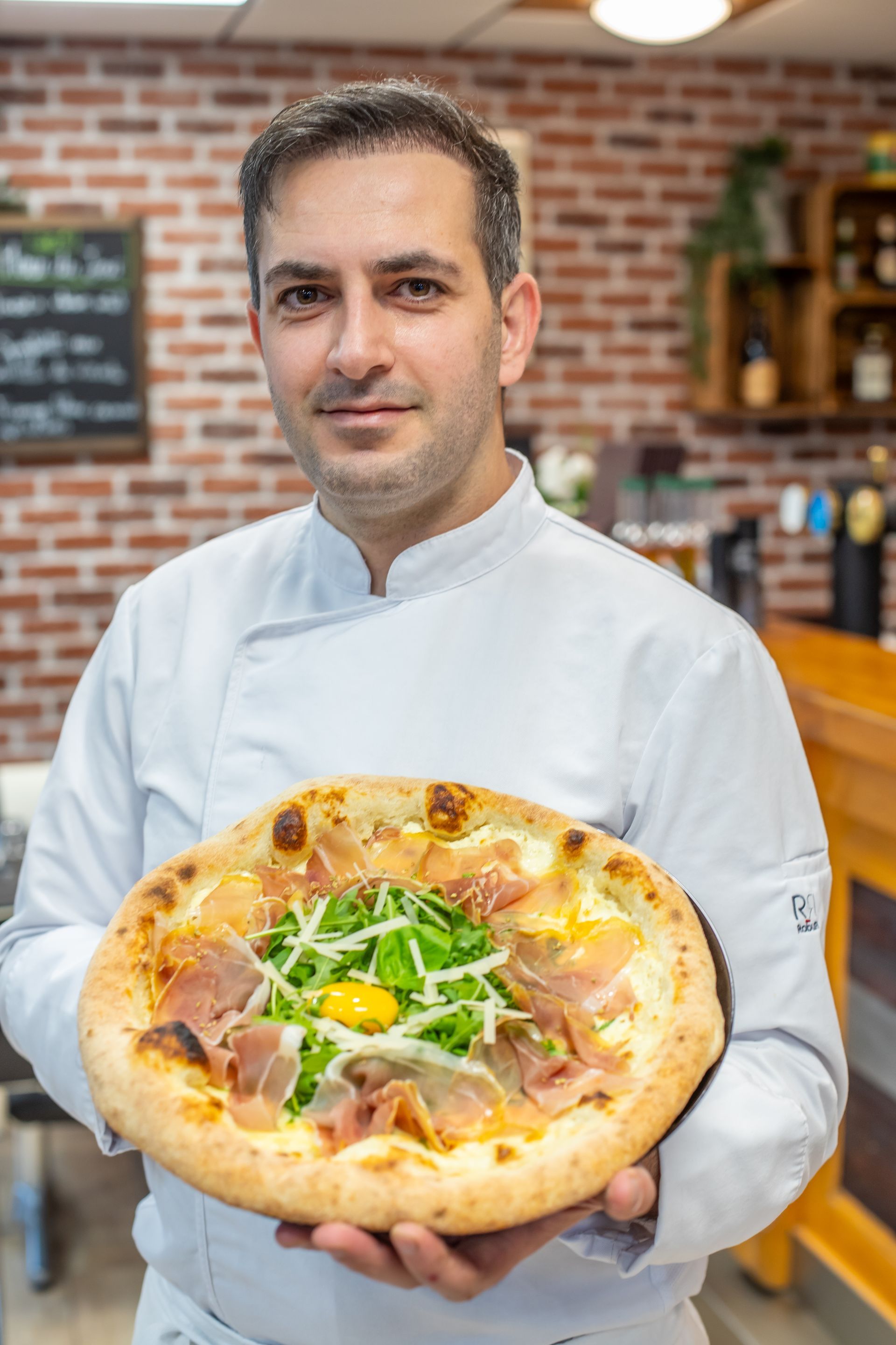 Des mains pétrissent la pâte, saupoudrent de farine et façonnent le pain sur une surface blanche, avec des particules de farine dans l'air.