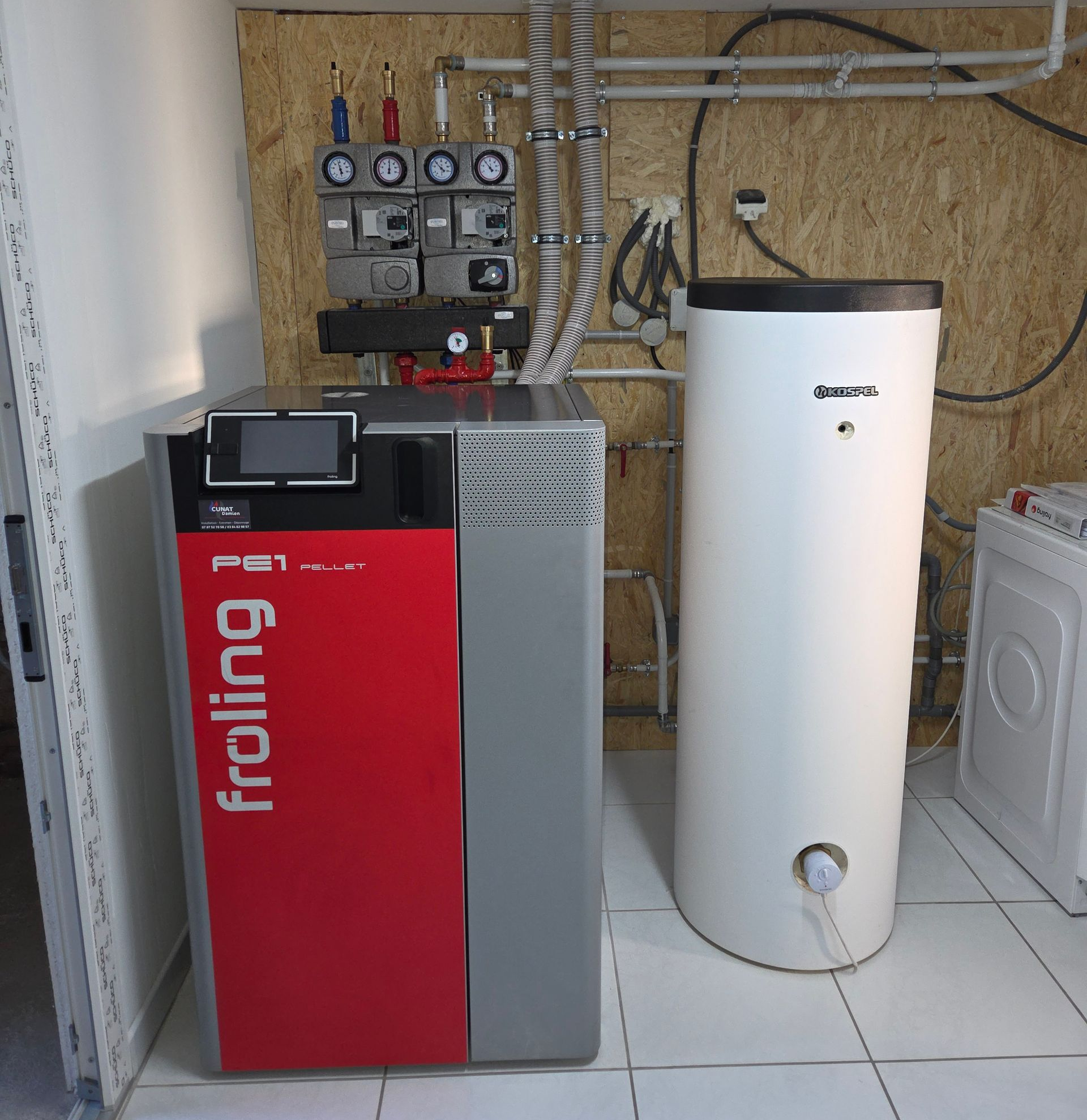 Unité de chauffage Froeling rouge et grise avec un réservoir d'eau blanche dans une buanderie.