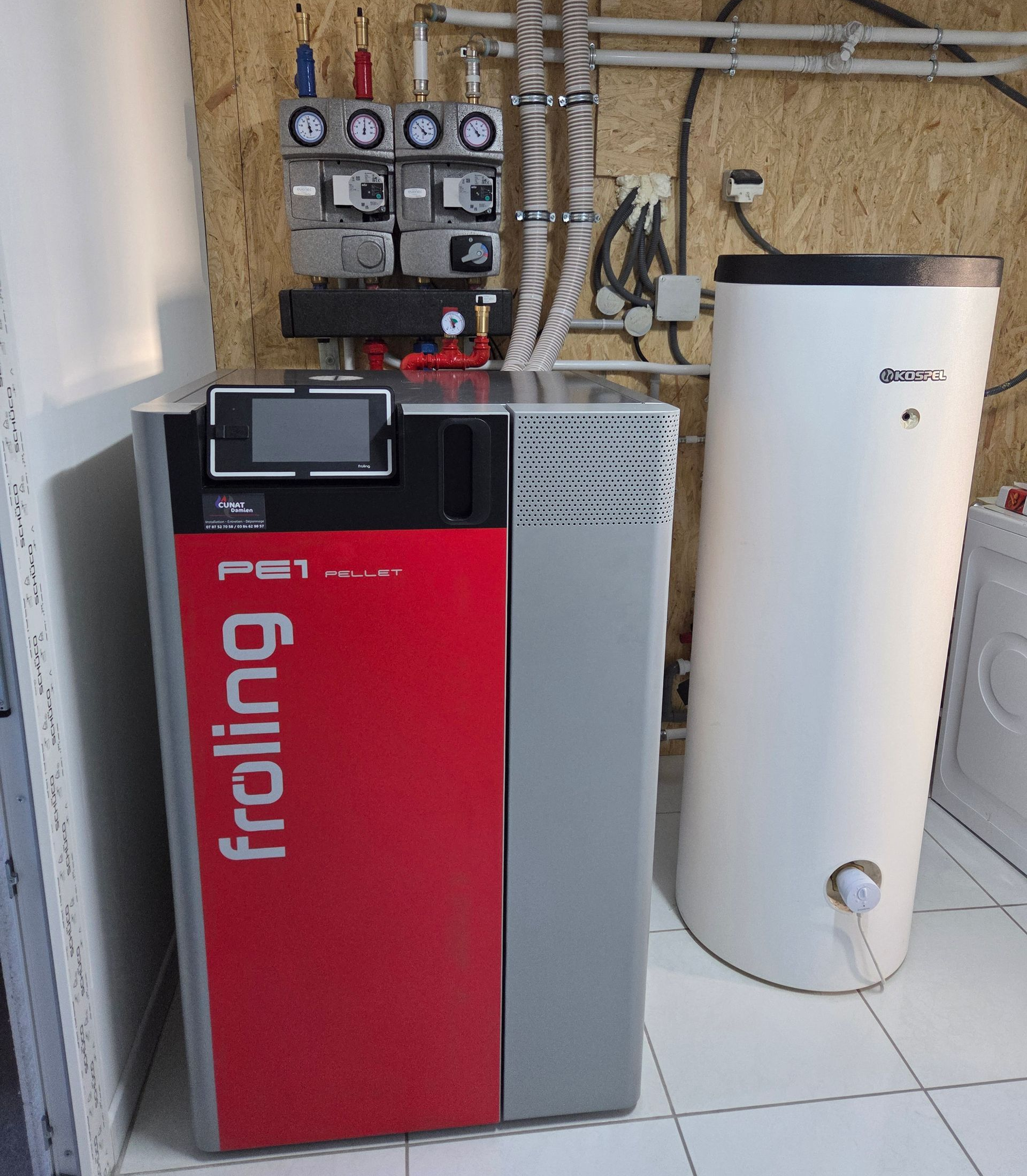 Chaudière à granulés Froling rouge et grise avec réservoir d'eau blanche et tuyauterie raccordée.