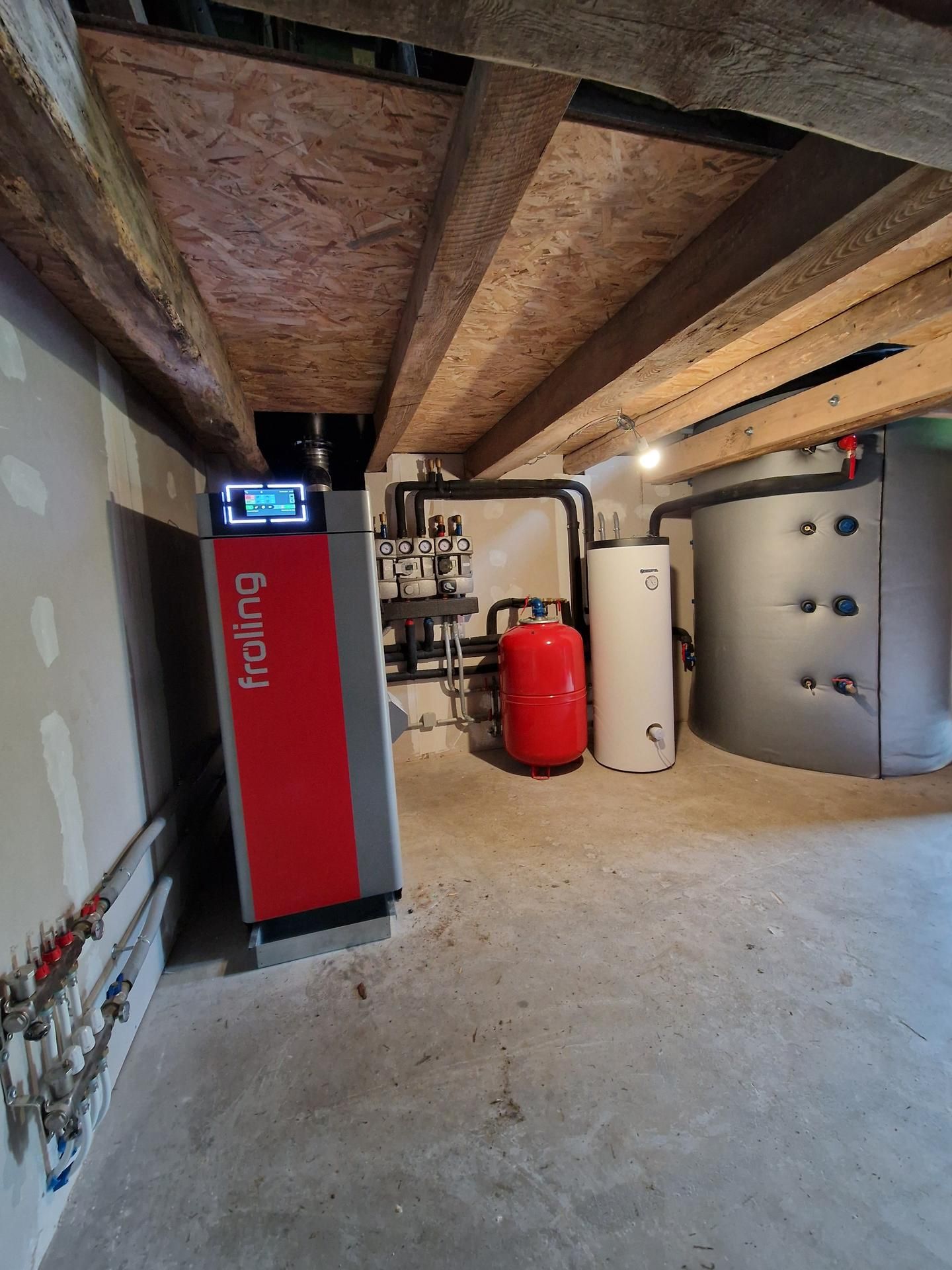 Système de chauffage Fröling rouge et gris dans un sous-sol avec divers tuyaux et réservoirs.