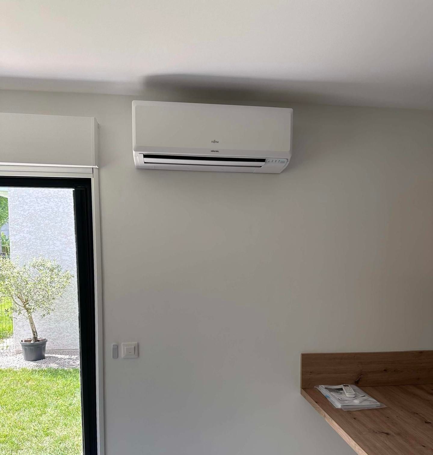 Climatiseur blanc monté sur un mur gris à côté d'une fenêtre.