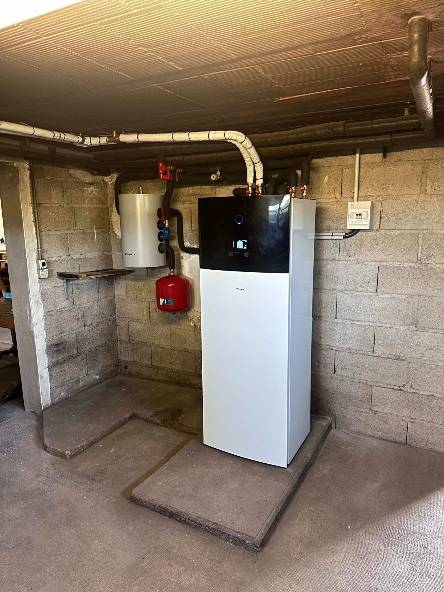 Unité de pompe à chaleur blanche et noire installée dans une pièce aux murs de briques avec tuyauterie et composants associés.