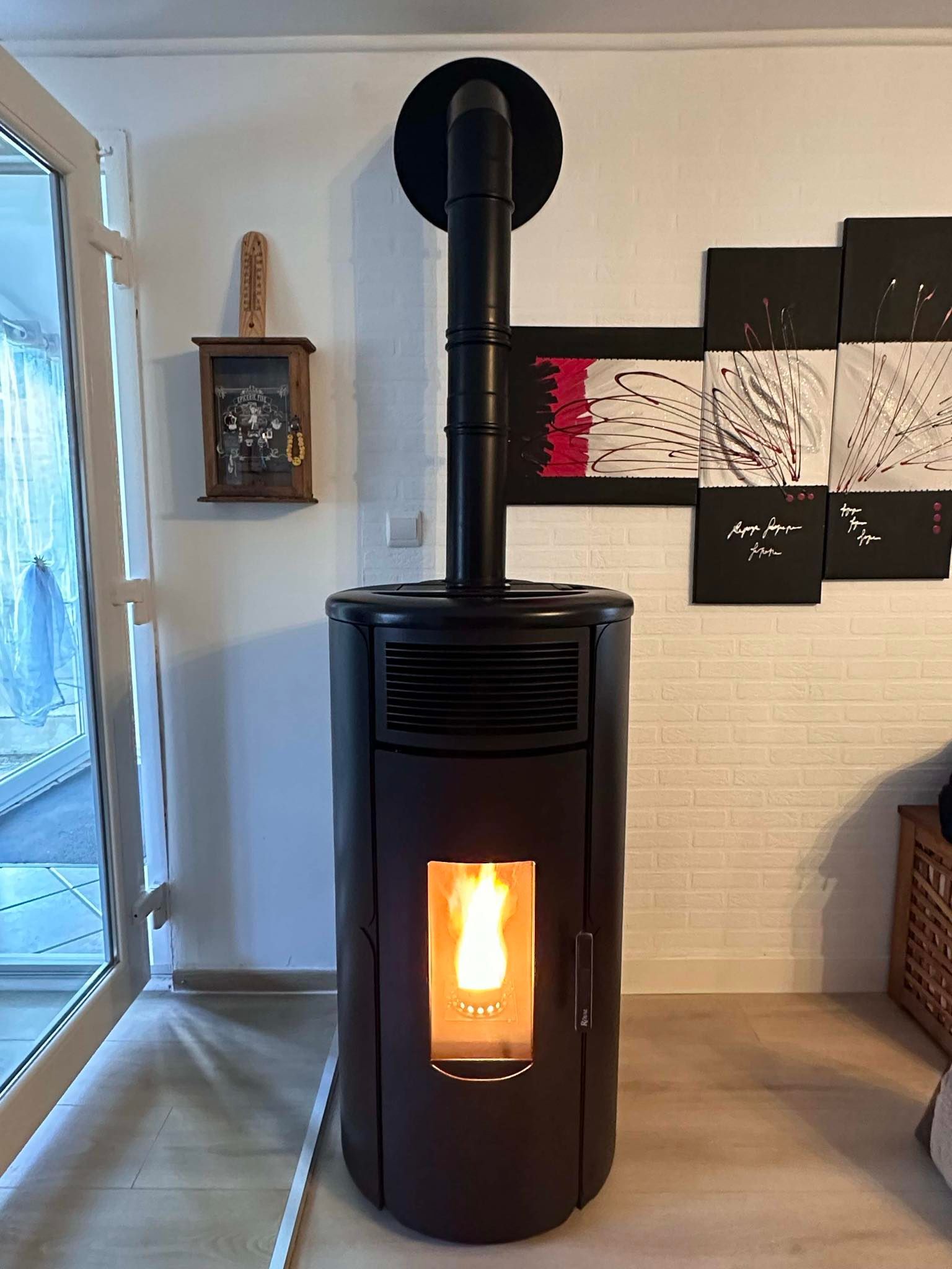Un poêle à granulés noir avec un feu rougeoyant, une cheminée et des œuvres d'art sur un mur de briques blanches.