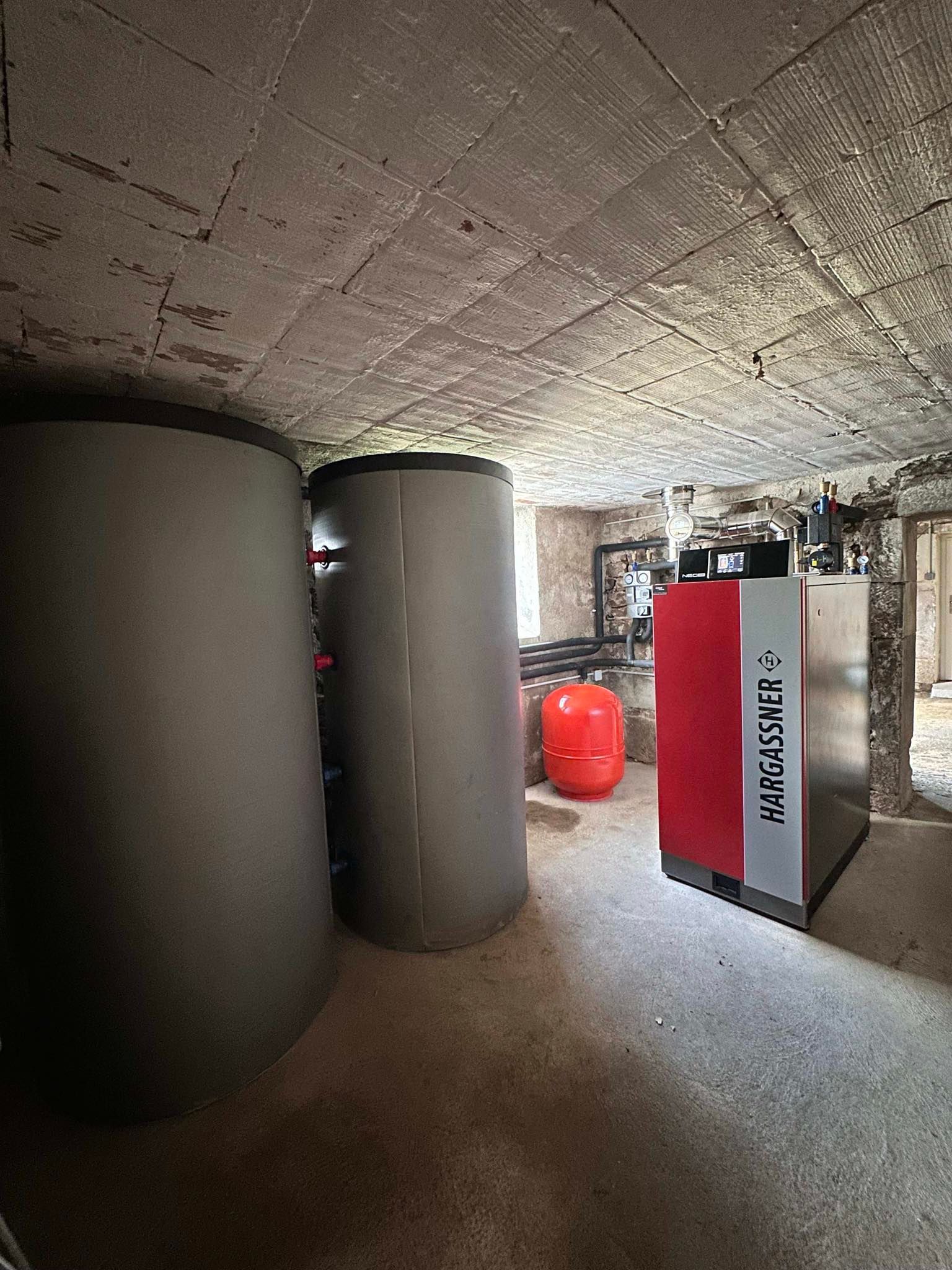 Deux grands réservoirs gris et une unité de chauffage rouge et grise dans un sous-sol.