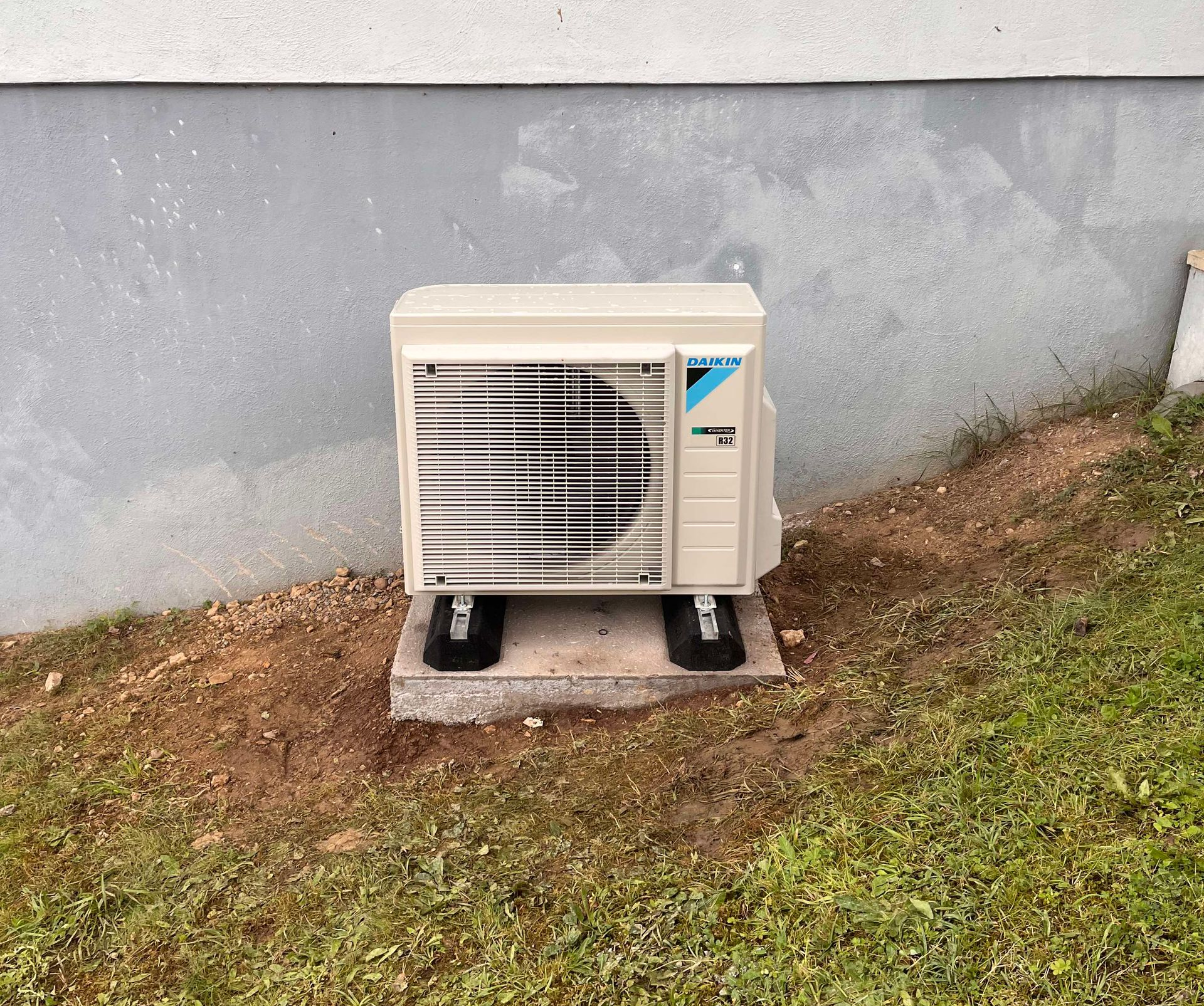 Unité de climatisation extérieure, beige, sur une dalle de béton à proximité d'un bâtiment.