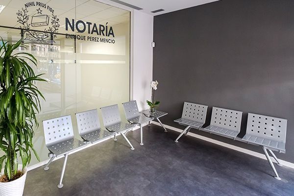 Sala de espera moderna para servicios notariales con sillas de metal gris, pared de cristal y maceta.