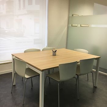 Pequeña sala de reuniones con una mesa de madera, cuatro sillas y paredes de vidrio esmerilado.