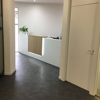 Pasillo de oficina moderno con mostrador de recepción blanco, paneles de madera y una planta en maceta.