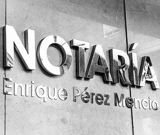 Metal sign reading “NOTARÍA Enrique Pérez Menco” on a stone wall.