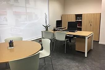 Oficina tranquila con mesa redonda, escritorio, sillas, armarios y una gran persiana.