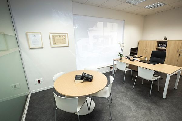 Sala de reuniones moderna con mesas redondas y rectangulares, sillas blancas y una gran pantalla mural.