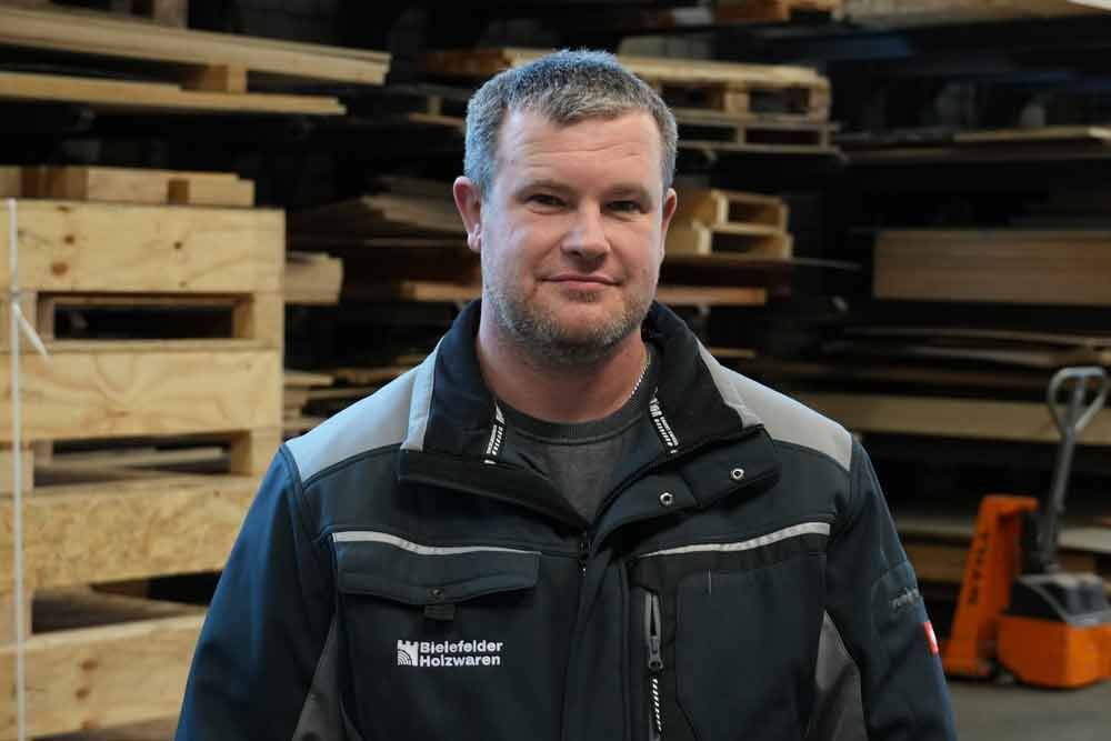 Ein Mann steht vor einem Stapel Holzpaletten.